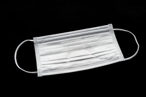 White surgical mask for protection against Coronavirus (COVID-19) and other contagious diseases. Close-up. Horizontal shot. Isolated on black background.